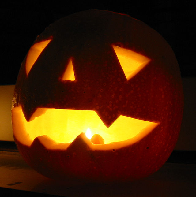 A lit orange jack o'lantern in shadows, facing toward the left. The jack o'lantern takes up most of the frame.